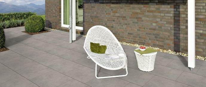 Moderne Terrasse mit großen grauen Fliesen, weißem Loungesessel, Beistelltisch und Blick auf die Berge.