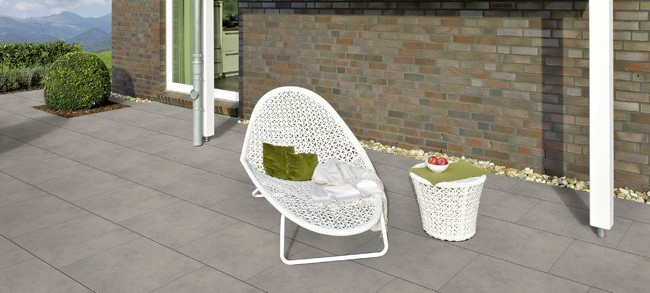 Moderne Terrasse mit großen grauen Fliesen, weißem Loungesessel, Beistelltisch und Blick auf die Berge.