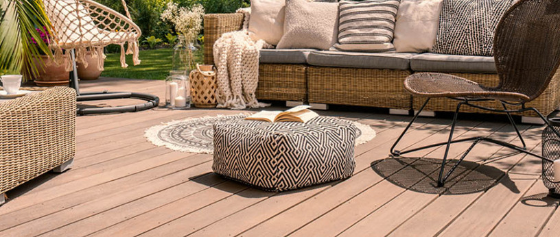 Gemütliche Terrasse mit Holz- oder WPC-Dielen, stilvollen Rattanmöbeln, Hängesessel, dekorativen Kissen und stimmungsvoller Gartengestaltung.