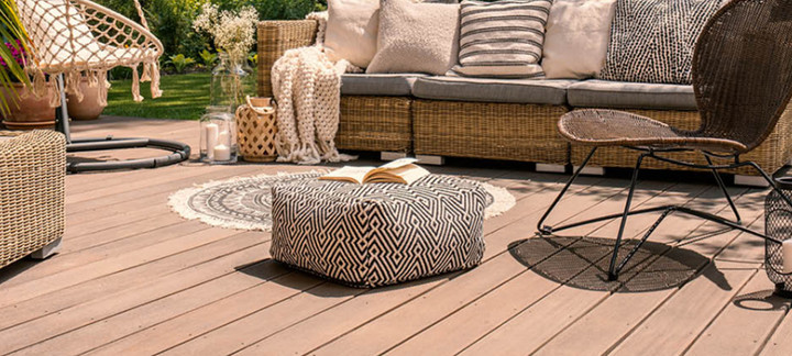 Gemütliche Terrasse mit Holz- oder WPC-Dielen, stilvollen Rattanmöbeln, Hängesessel, dekorativen Kissen und stimmungsvoller Gartengestaltung.