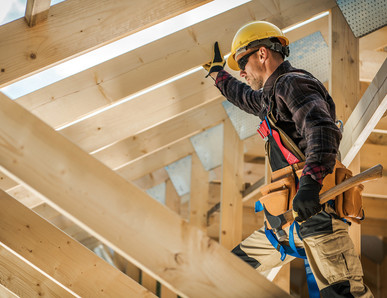 Zimmermann mit Schutzhelm und Werkzeug befestigt Konstruktionsvollholz (KVH) beim Bau eines Dachstuhls.