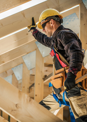 Zimmermann mit Schutzhelm und Werkzeug befestigt Konstruktionsvollholz (KVH) beim Bau eines Dachstuhls.
