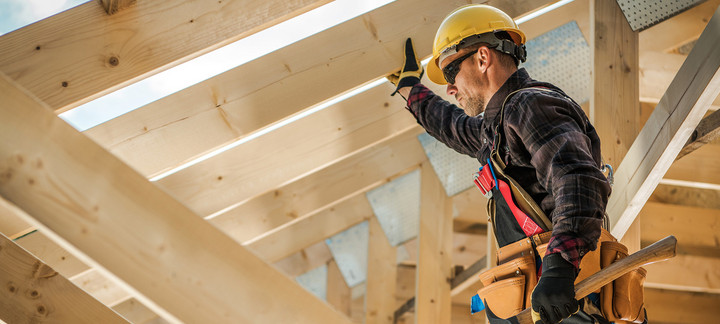 Zimmermann mit Schutzhelm und Werkzeug befestigt Konstruktionsvollholz (KVH) beim Bau eines Dachstuhls.