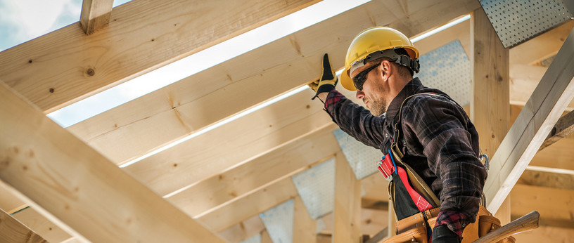 Zimmermann mit Schutzhelm und Werkzeug befestigt Konstruktionsvollholz (KVH) beim Bau eines Dachstuhls.